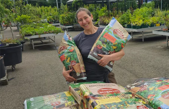 frau hält zwei säcke erde und lacht in die kamera