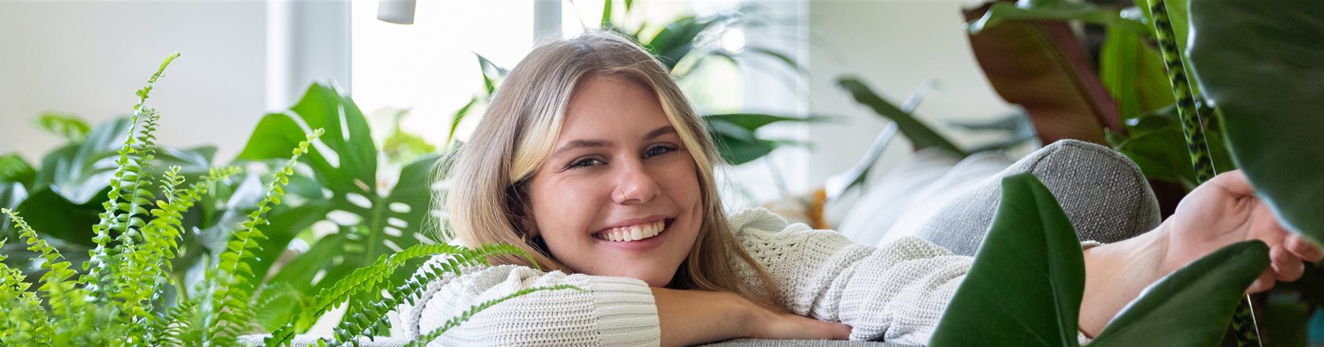 Jungle Ambiente - Frau liegt auf Sofa zwischen Grünpflanzen